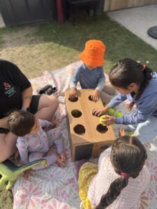 Tamariki at Growing Wings putting a tennis ball into a wooden box with holes showcasing trajectory