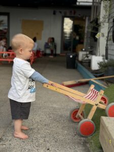 Child at Growing Wings transporting a wooden toy cart from one location to another