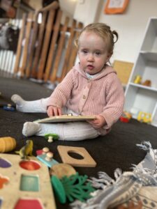 A toddler at a Growing Wings centre sitting on the floor exploring and playing with toys to get a feel of the daily rhythm